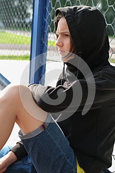Handsome teenager boy sitting near net fence