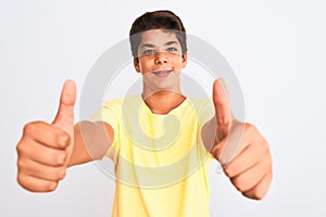 Handsome teenager boy standing over white isolated background approving doing positive gesture with hand, thumbs up smiling and