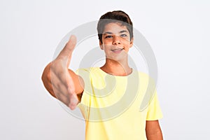 Handsome teenager boy standing over white isolated background smiling friendly offering handshake as greeting and welcoming