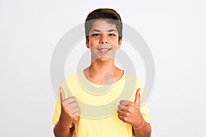 Handsome teenager boy standing over white isolated background success sign doing positive gesture with hand, thumbs up smiling and