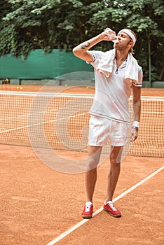 handsome tennis player with towel drinking water