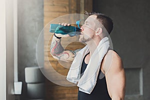 Handsome thirsty young man in gym, drinking water from bottle