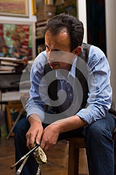 Handsome thoughtful male artist sitting painting in a studio