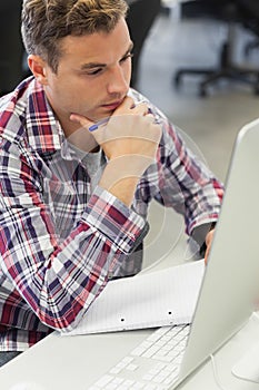 Handsome thoughtful student using computer taking notes