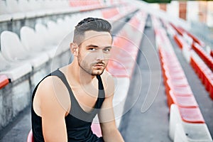 Handsome tired athlete relaxing on stadium stairs after workout