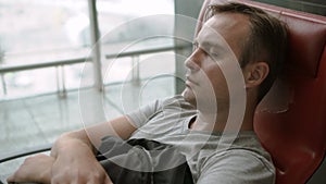 Handsome tired young man sleeping in airport terminal. Long distance connected flights jet-lag.