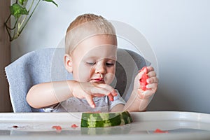 Handsome toddler boy eating juicy ripe watermelon at home at highchair