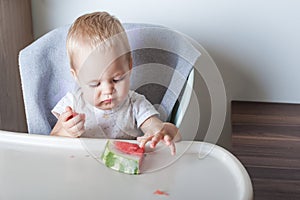 Handsome toddler boy eating juicy ripe watermelon at home at highchair