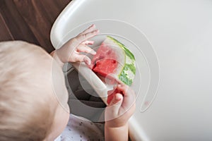 Handsome toddler boy eating juicy ripe watermelon at home at highchair