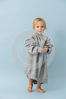 Handsome toddler boy in a huge oversized grey longsleeve over blue