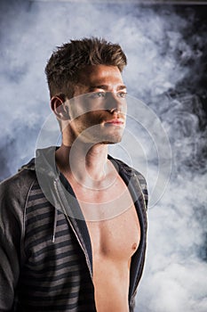 Handsome tough young man in dark hoodie on smoky
