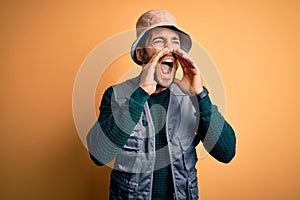 Handsome tourist man with beard on vacation wearing explorer hat over yellow background Shouting angry out loud with hands over