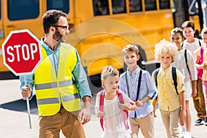 handsome traffic guard crossing road with pupils in front of