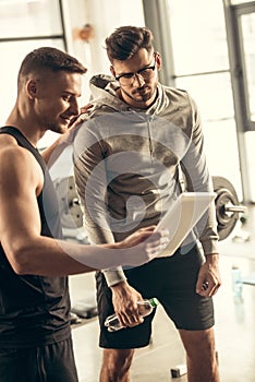 handsome trainer showing results of exercising on tablet to exhausted sportsman