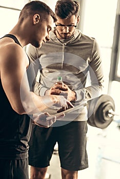 handsome trainer showing results of exercising on tablet to sportsman