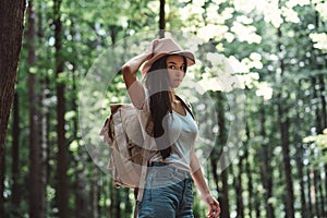 Handsome traveler hipster girl with backpack and hat walking in forest among trees