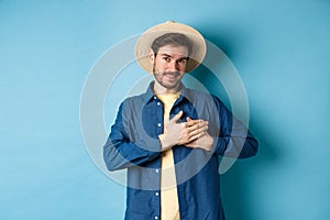 Handsome traveler in straw hat, holding hands on heart and smiling, showing thank you gesture, keep memories about