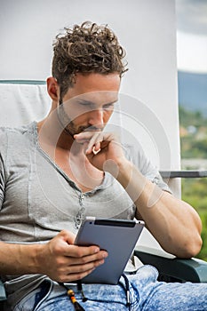 Handsome trendy man looking down at a tablet computer, outdoor