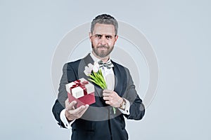 handsome tuxedo man hold gift box and tulip flowers, birthday