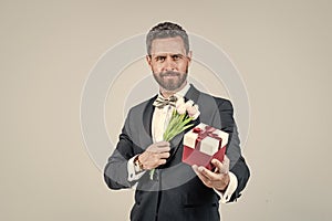 handsome tuxedo man hold gift box and tulip flowers, birthday