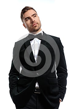 Handsome unshaved man in black tuxedo holding hands in pockets