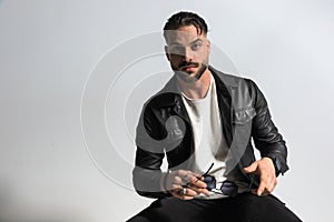 Handsome unshaved man with wet hair in leather jacket holding sunglasses