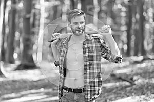 Handsome unshaven lumberjack with sexy torso in open plaid shirt hold large axe in strong hands summer wood, fit