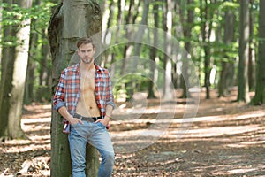 Handsome unshaven man with lumbersexual look in unbuttoned lumberjack shirt forest background