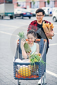 Handsome vietnamese man holds paper bags with food pushing in front of him shopping trolley with his happy beautiful