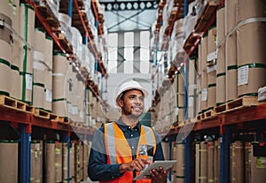 Handsome warehouse worker uses digital tablet for checking stock, on the shelves standing cardboard boxes