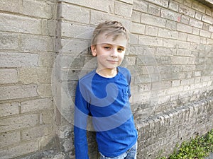 A handsome white boy in a blue sweater or longsleeve is smiling. Child on a brick wall background. On the face is an emotion of