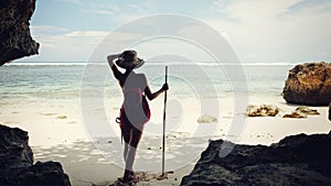 Handsome woman on the beach with hat, stick and backpack