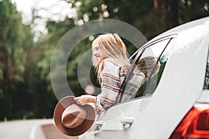 Handsome woman hanging out of the car window, hold vintage hat and enjoying beautiful road