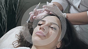 Handsome woman receives an injection in the head. The procedure makes doctor in white gloves. The concept of mesotherapy