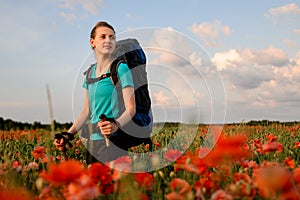 Handsome woman tourist stands on field of red poppies.