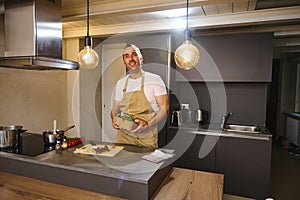 Handsome young adult man 40s, in beige chef apron holding a cardboard crate with fresh green leaves of arugula, smiling