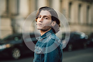 Handsome young adult man on city street wearing casual denim jeans shirt.