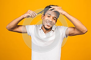 Handsome young african american black man combing his hair in bathroom. Isolated over yellow background