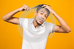 Handsome young african american black man combing his hair in bathroom. Isolated over yellow background