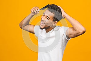 Handsome young african american black man combing his hair in bathroom. Isolated over yellow background