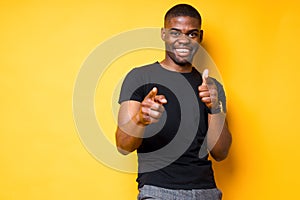 Handsome young african american guy in a black t-shirt points his finger at the camera and raises his thumb up