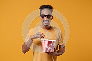 Handsome young african american guy in 3d imax glasses posing isolated on yellow orange background in studio. People photo