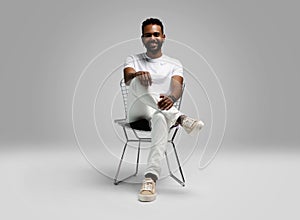 Handsome young african american guy sitting on stool, posing in studio - isolated