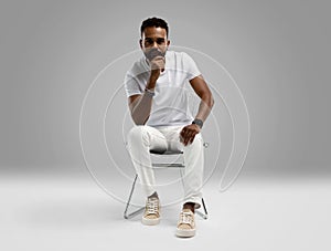 Handsome young african american guy sitting on stool, posing in studio - isolated