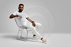 Handsome young african american guy sitting on stool, posing in studio - isolated