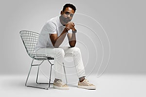 Handsome young african american guy sitting on stool, posing in studio - isolated