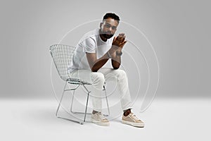 Handsome young african american guy sitting on stool, posing in studio - isolated