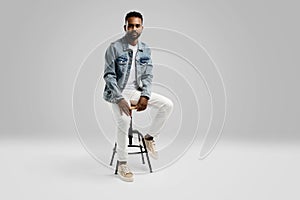 Handsome young african american guy sitting on stool, posing in studio - isolated