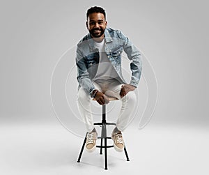 Handsome young african american guy sitting on stool, posing in studio - isolated