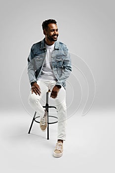 Handsome young african american guy sitting on stool, posing in studio - isolated